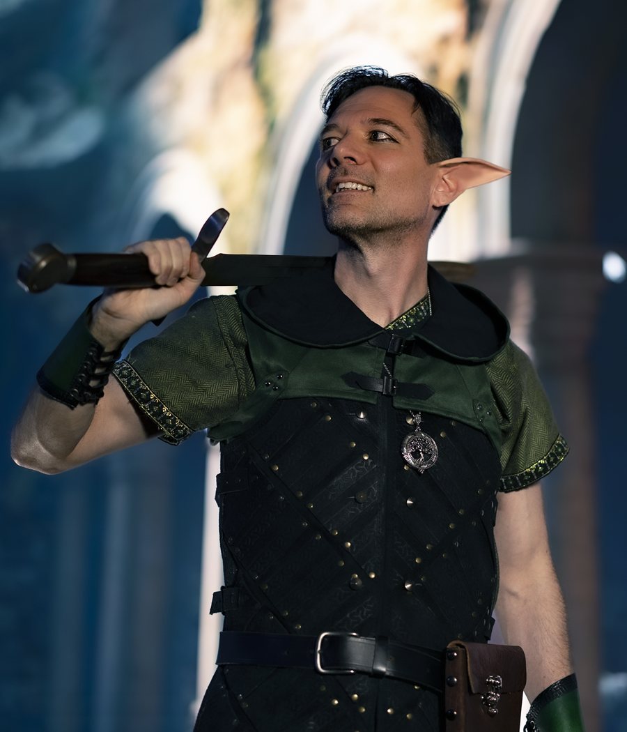 A player in elf ears and green and black leather armor, a sword resting on his shoulder